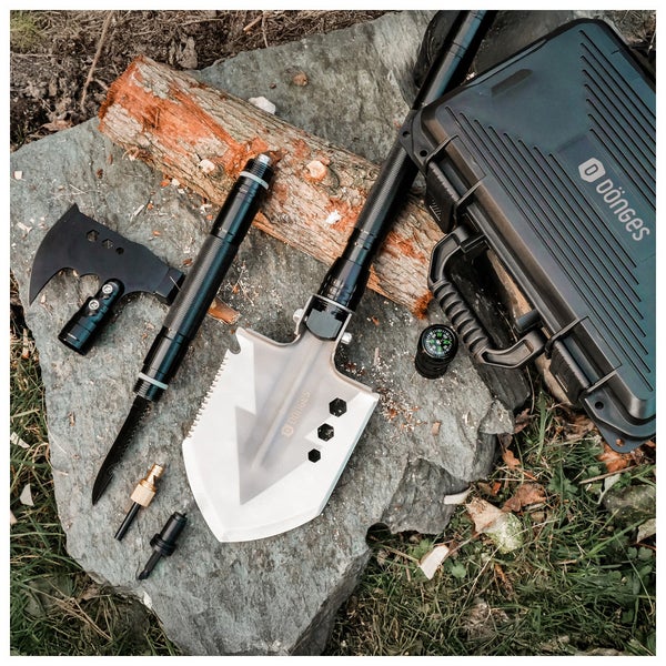 Organisiertes taktisches Dönges Überlebens-Set mit Klappschaufel, Axt, Messer und Kompass auf einem Stein neben einem Koffer mit Dönges Logo.
