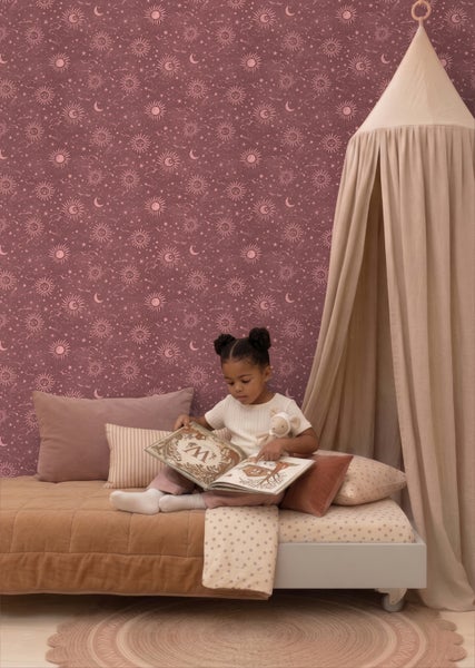 Kinderzimmer mit gemusterter Tapete mit Sonne, Mond und Sternen, einem niedrigen Bett mit Kissen und einem Baldachin.