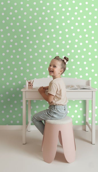 Mädchen sitzt an Schreibtisch vor Wand mit Punktmuster-Tapete