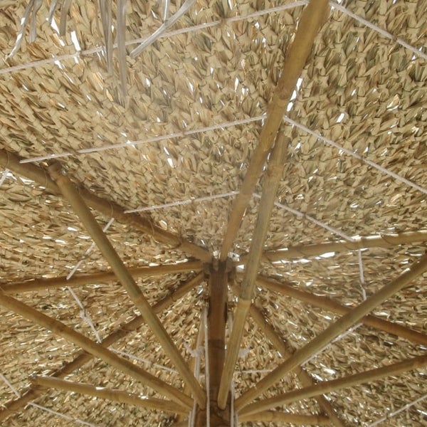 Detailansicht eines Sonnenschirms aus Naturmaterialien mit Holzstab