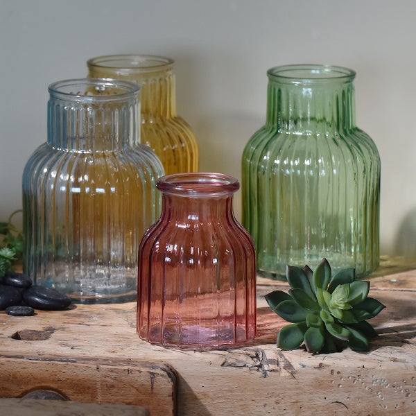Vier geriffelte Glasvasen in verschiedenen Farben auf einer Holzoberfläche mit einer Sukkulente und Dekosteinen.