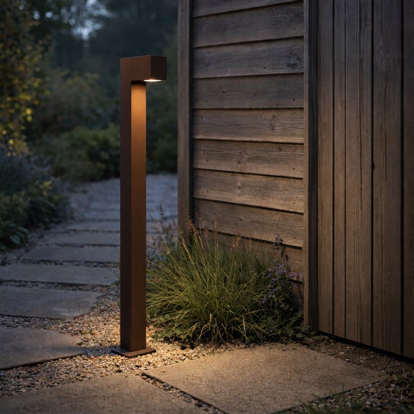 Moderne LED-Wegeleuchte in Dunkelbraun an einem Gartenweg neben einer Holzwand, die den Boden mit warmem Licht beleuchtet.