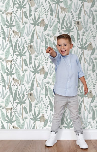 Ein Junge steht vor einer Wand mit einer Dschungeltapete mit Pflanzen und Affenmotiven.