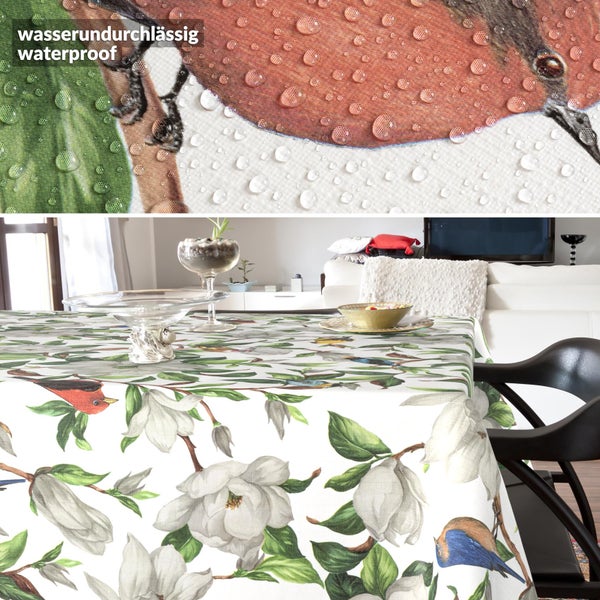 Wasserdichte Tischdecke mit Magnolien- und Vogelmuster in hellem Wohnzimmer, Detailansicht zeigt abperlende Wassertropfen auf der Oberfläche.