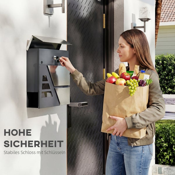 Eine Frau öffnet einen modernen Wandbriefkasten aus Metall mit einem Schlüssel an einer Hauswand neben einer Eingangstür.