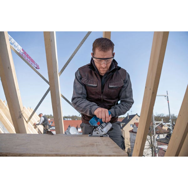 Handwerker mit Schutzbrille sägt Holz mit einer Mini-Handkreissäge auf einer Baustelle