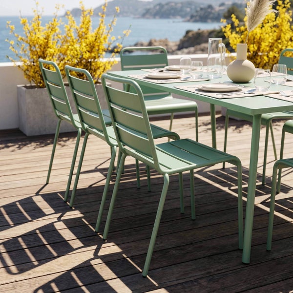 Helle Gartenmöbelgruppe aus grünem Metall mit modernem Esstisch und Lattenstühlen auf einer Holzterrasse im Freien.