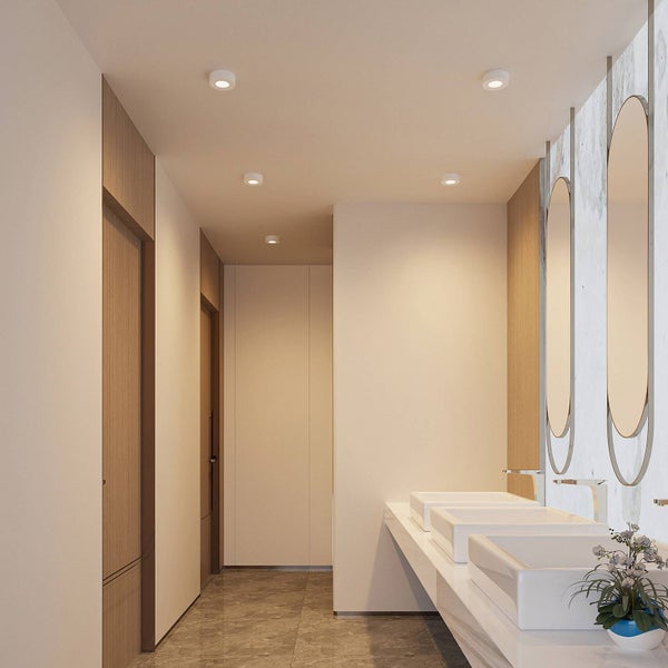 Modernes, helles Badezimmer mit runden Deckenaufbaustrahlern, drei Waschbecken und ovalen Spiegeln vor einer Wand in Marmoroptik.