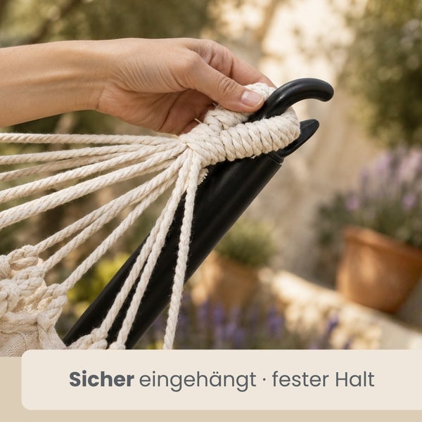 Hand fixiert die Seilschlaufe einer Hängematte sicher an einem schwarzen Metallständer.