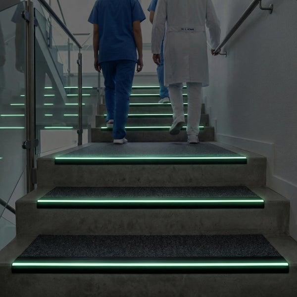 Treppenstufen mit selbstleuchtenden Kantenschutzprofilen in einem Krankenhausflur mit Personen auf der Treppe