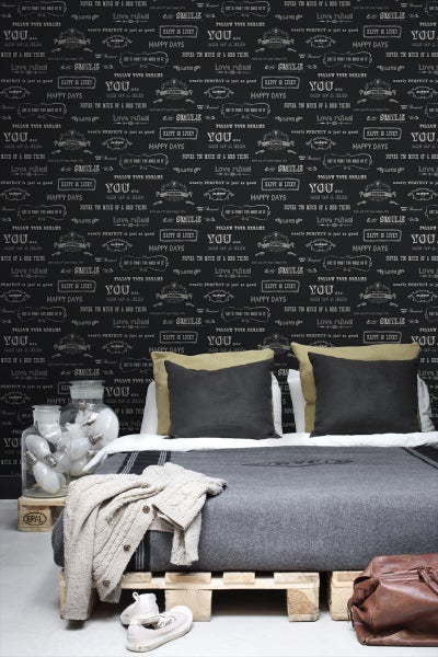 Schlafzimmer mit Bett auf Paletten und Wandtapete mit Schriftzug