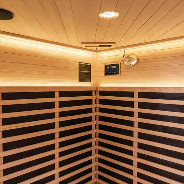 Moderne Ecksauna von Home Deluxe mit Glasfront und Innenbeleuchtung in einem Badezimmer, eine Frau sitzt in der Sauna, ein Mann steht davor.