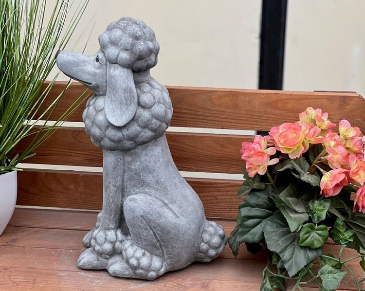 Gartenfigur Pudel aus Steinguss in sitzender Position auf einer Holzbank neben einer Kunstpflanze.