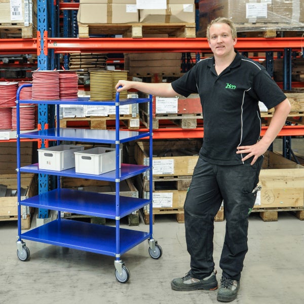 Blauer Transportwagen mit vier Regalböden und einem Mitarbeiter in einem Lager