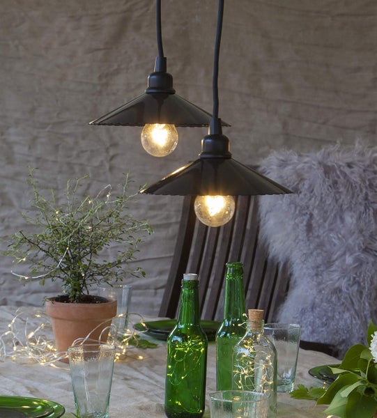 Dekorativer Tisch mit zwei Pendelleuchten, Flaschen mit Lichterketten, Pflanze und Gläsern.