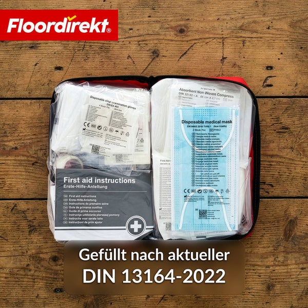 Floordirekt Logo. Offene Erste-Hilfe-Tasche mit medizinischen Masken, Handschuhen und Verbandsmaterial nach der Norm DIN 13164-2022.