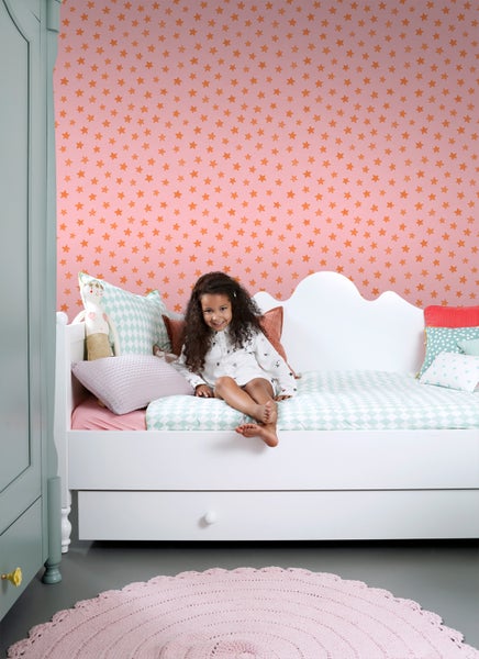 Kinderzimmer mit Mädchen auf Bett vor Sternentapete, Kleiderschrank und Teppich