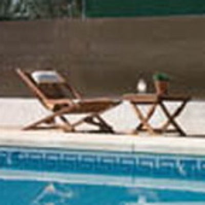 Sonnenliege aus Holz und kleiner Beistelltisch am hellen Poolrand. Klassische Gartenmöbel aus braunem Holz.