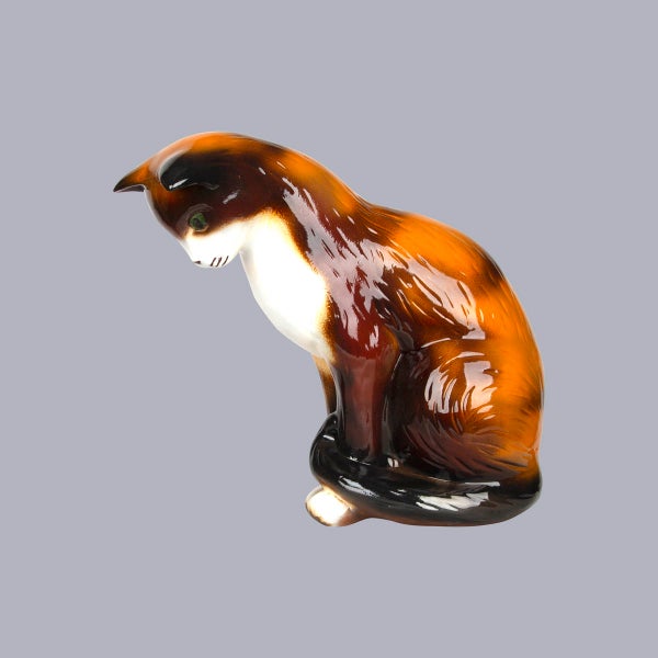 Sitzende Katzenfigur aus glasierter Keramik, braun, schwarz und weiß.