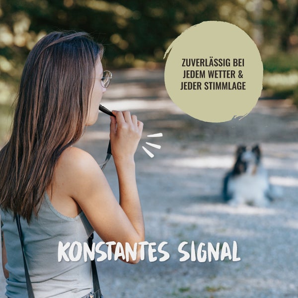 Eine Frau benutzt eine Hundepfeife in der Natur, während ein Hund im Hintergrund wartet. Auf dem Bild sind die Texte 'Zuverlässig bei jedem Wetter & jeder Stimmlage' und 'Konstantes Signal' abgebildet.