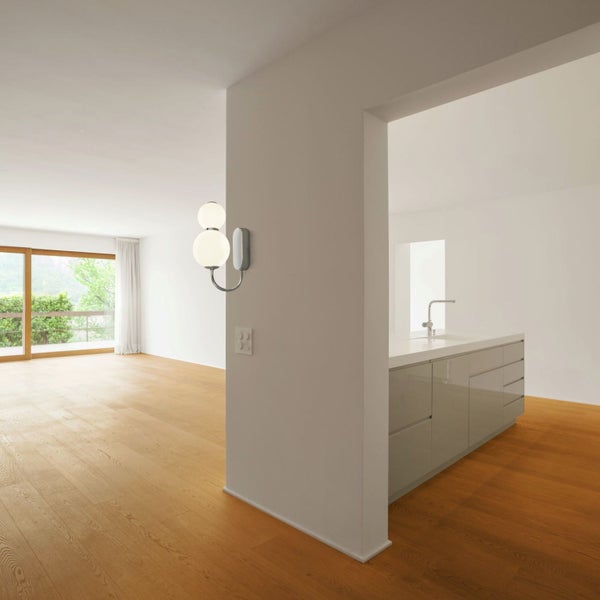 Heller Wohnraum mit Wandleuchte, Holzboden und Küchenzeile.