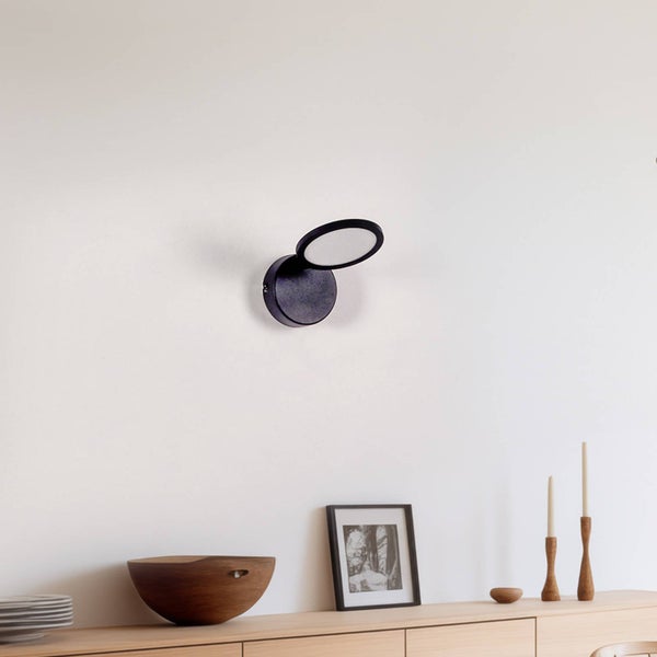 Moderne schwarze Wandleuchte mit verstellbarem ringförmigem Leuchtmittel, montiert über einem Sideboard aus Holz in einem hellen Raum.