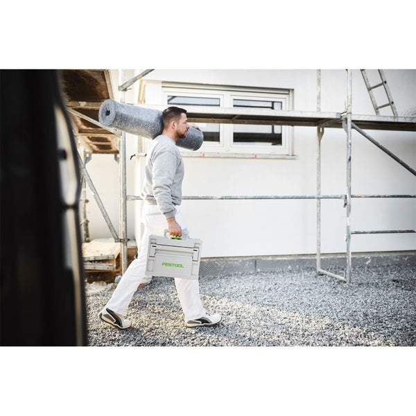 Handwerker mit Werkzeugkoffer und Materialrolle vor einem Haus mit Gerüst