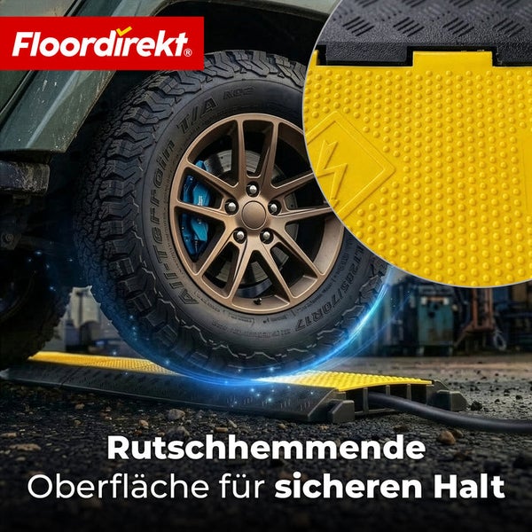 Fahrzeugreifen überfährt eine schwarz-gelbe Kabelbrücke mit rutschhemmender Oberfläche für sicheren Halt. Floordirekt Logo.