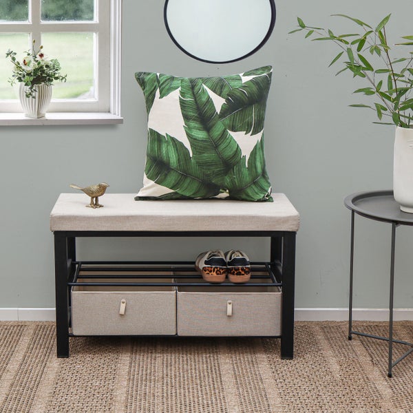 Moderne Schuhbank aus schwarzem Metall mit beigem Sitz, zwei Schubladen und Ablage in hellem Raum mit Teppich, Pflanzen und Dekokissen.