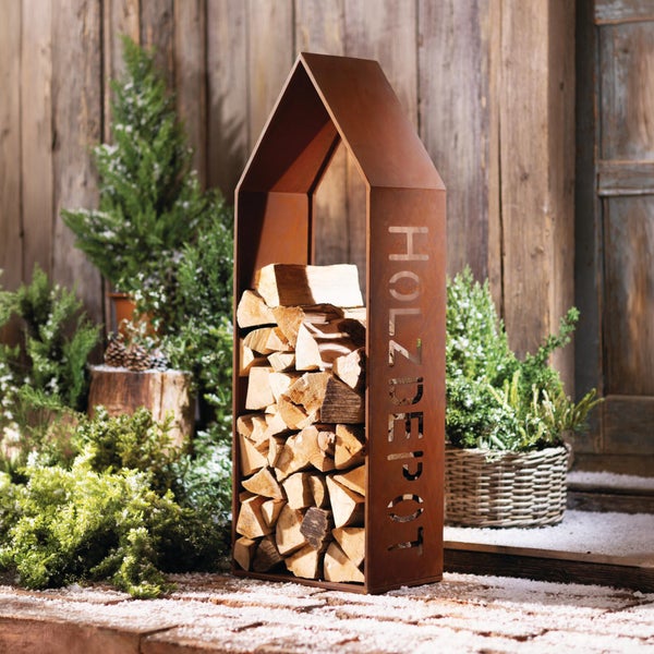 Kaminholzregal aus Metall mit Edelrost Patina in Hausform mit der Aufschrift Holzdepot befüllt mit Kaminholz vor einer winterlichen Kulisse