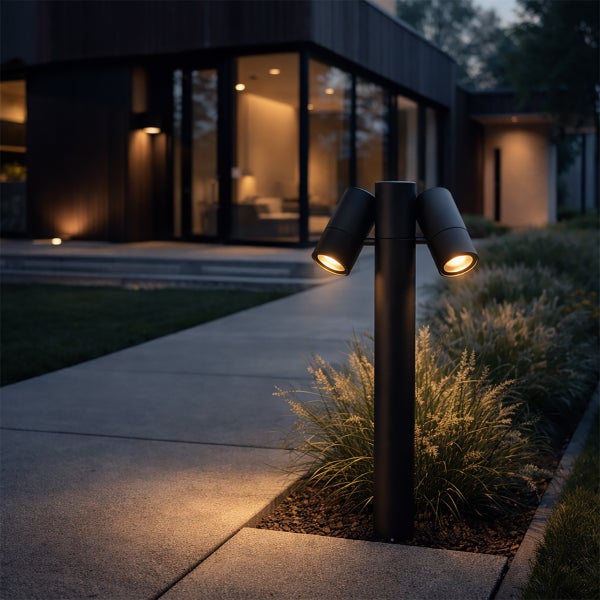 Moderne Außenleuchte mit zwei verstellbaren Spots an einem Gartenweg vor einem beleuchteten Haus bei Dämmerung.
