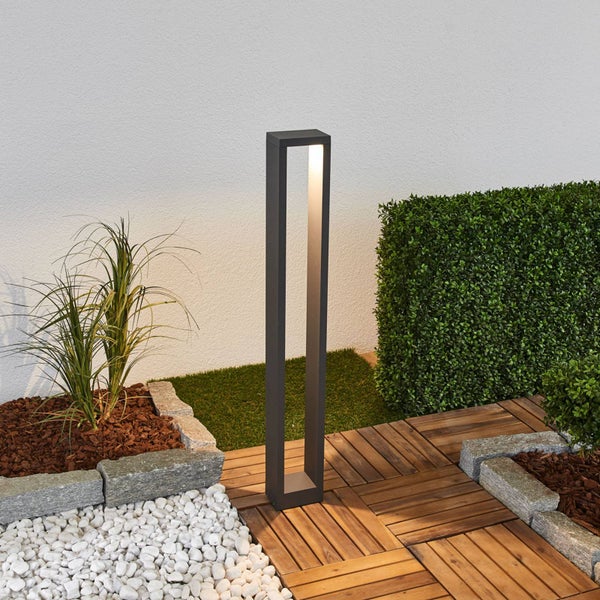 Moderne LED-Sockelleuchte in einem organisierten Garten mit Holzfliesen, weißen Kieseln und einer grünen Hecke.
