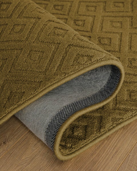 Strukturierter Teppich mit geometrischem Rautenmuster und sichtbarer Rückseite auf Holzboden.
