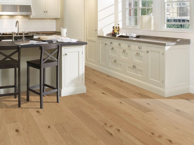 Helle Küche im Landhausstil mit Parkettboden aus Eichenholz, weißer Küchenzeile und einer Kücheninsel mit dunklen Barhockern.