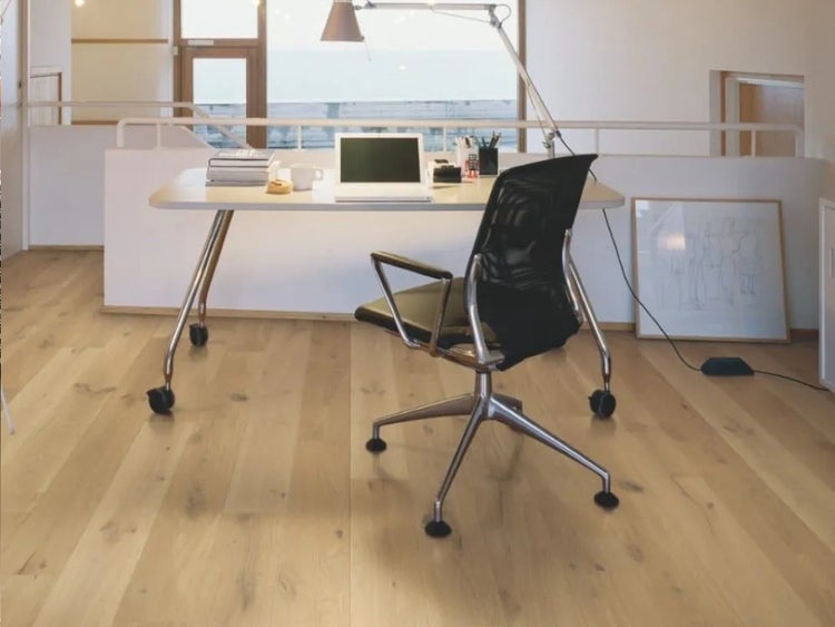 Helles Arbeitszimmer mit Parkettboden aus Holz. Die moderne Einrichtung umfasst einen weißen Schreibtisch und einen schwarzen Bürostuhl.