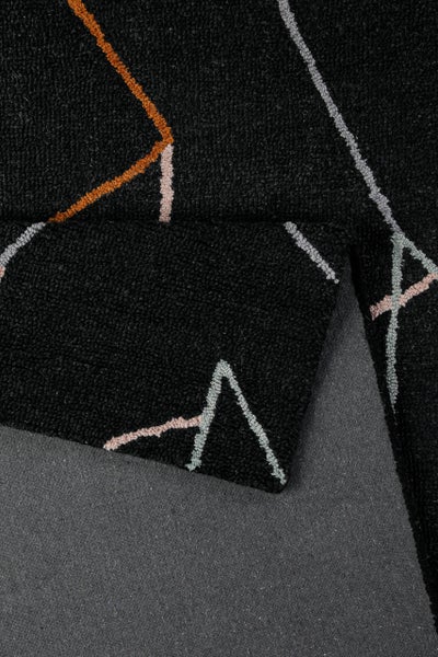 Nahaufnahme eines schwarzen Teppichs mit geometrischem Muster aus farbigen Linien und einer umgeschlagenen Ecke mit grauer Rückseite.