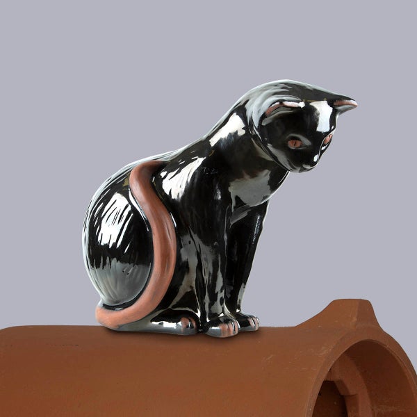 Schwarze Firstfigur Katze aus glasierter Keramik auf einem Dachziegel sitzend.