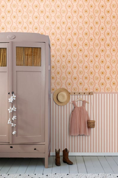 Kinderzimmer mit Motivtapete mit Sonnen und Streifen, einem rosa Holzschrank, einer Garderobenleiste mit Hut und Kleidung sowie Stiefeln.