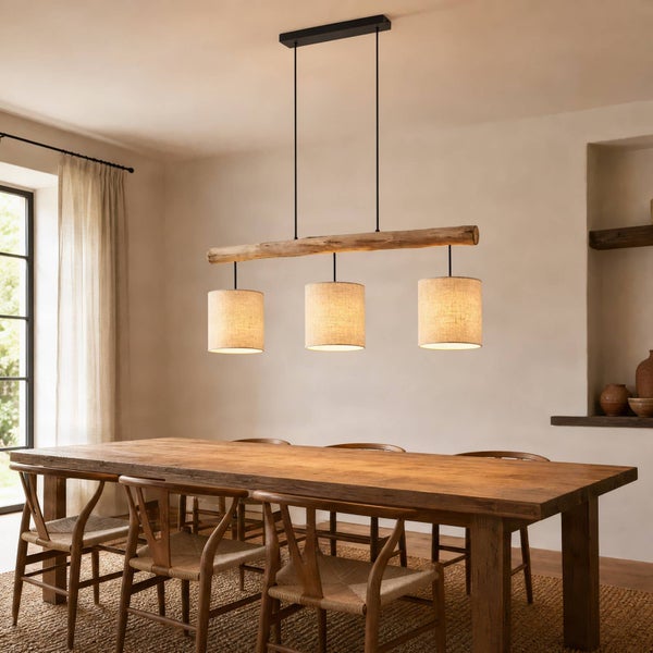 Moderne Pendelleuchte mit Holzbalken und drei zylindrischen Stoffschirmen über einem Holzesstisch in einem hellen, rustikal eingerichteten Raum.