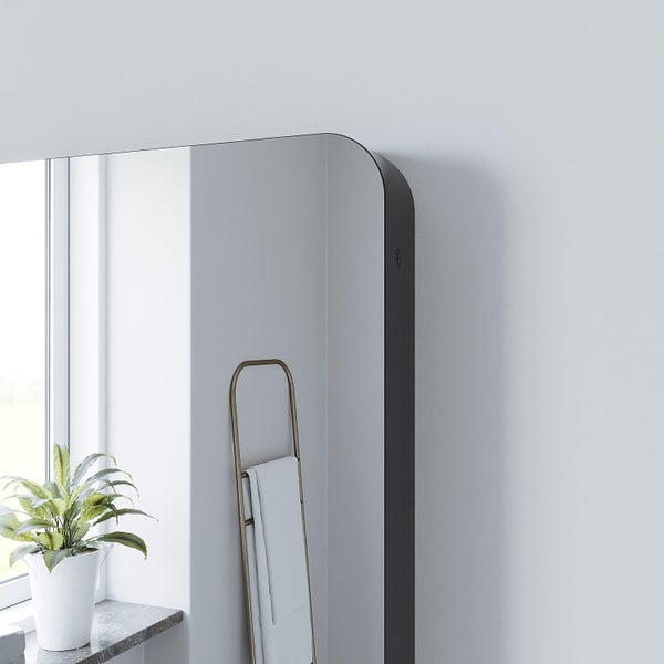 Wandspiegel mit abgerundeter Ecke und dunklem Rahmen in einem modern eingerichteten Badezimmer neben einem Handtuchhalter