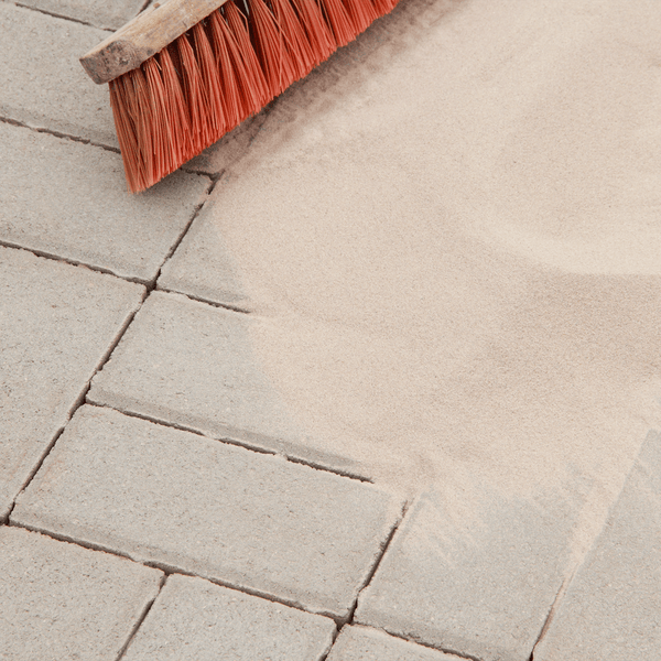 Einkehren von Fugensand mit einem Besen in die Fugen von Pflastersteinen auf einer Terrasse.