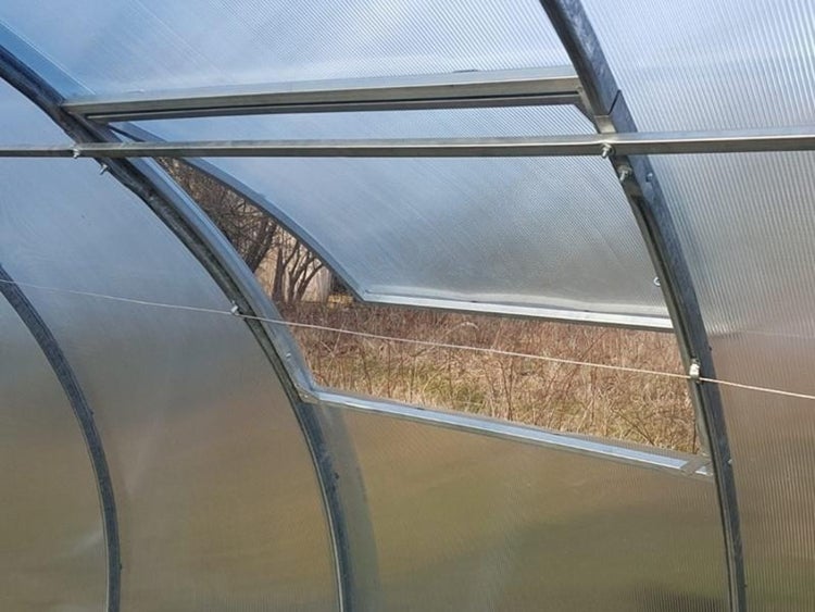 Geöffnetes Dachfenster in einem Gewächshaus mit Metallrahmen und transparenten Stegplatten