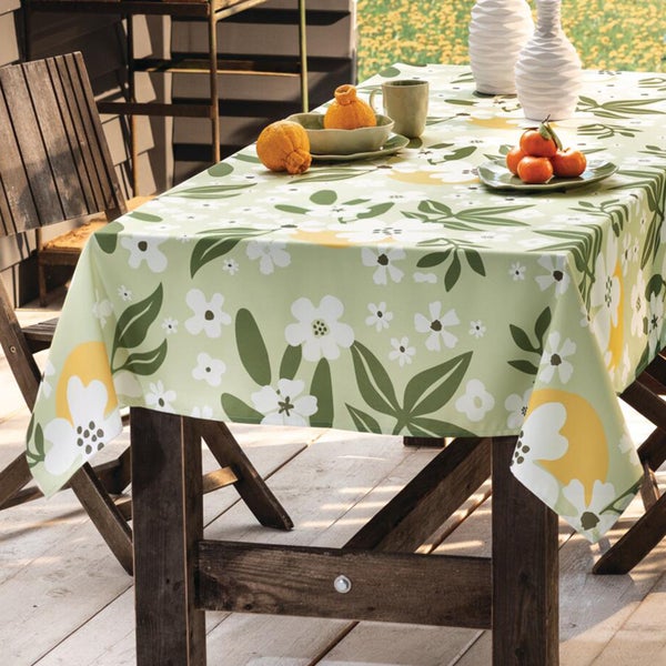 Hell gestalteter Außenbereich mit einem Holztisch und einer gemusterten Tischdecke mit Blumen und Zitronen auf einer Holzterrasse.