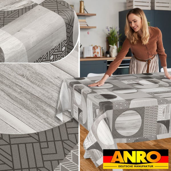Eine Frau breitet eine abwaschbare Tischdecke mit geometrischen Mustern und Holzoptik auf einem Küchentisch aus. ANRO DEUTSCHE MANUFAKTUR Logo.