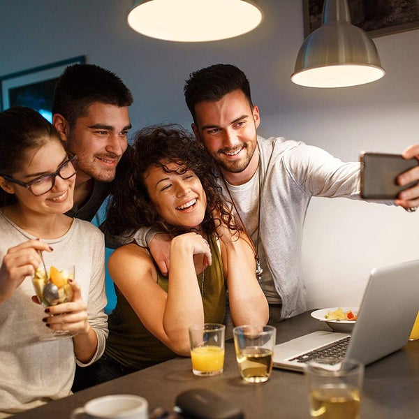 Vier lächelnde Personen an einem Tisch mit Laptop unter dem warmen Licht von zwei runden Pendelleuchten.