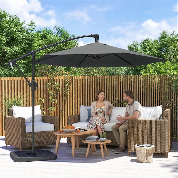 Großer grauer Ampelschirm über einer modernen Gartenlounge aus Polyrattan mit beigen Polstern auf einer hellen Steinterrasse vor einem Holzzaun.
