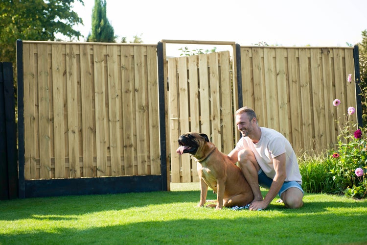 Mann mit Hund vor einem Holzzaun im Garten.