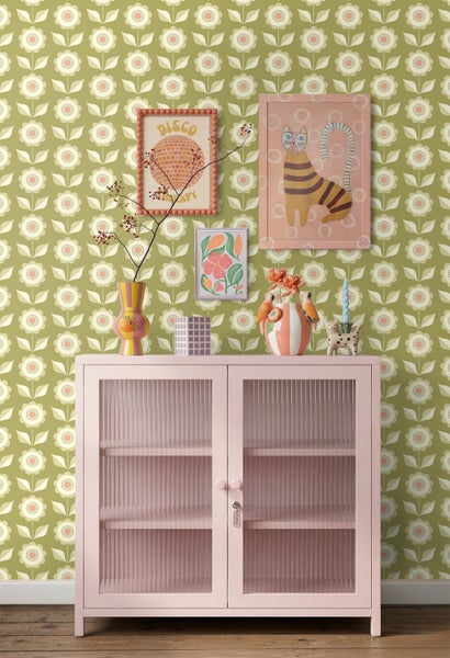 Vliestapete mit retro Blumenmuster in Olivgrün hinter einer rosafarbenen Vitrine mit Dekoration.