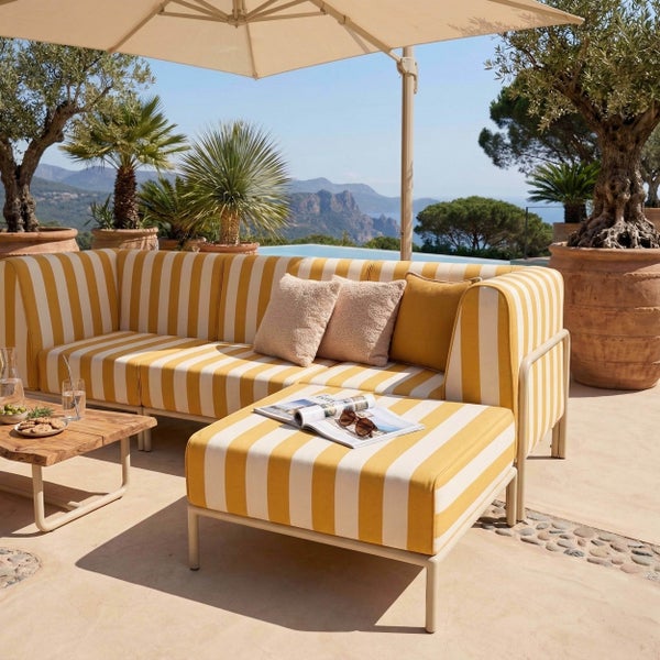 Gestreifte Outdoor-Lounge mit Sofa, Hocker und Holztisch auf einer hellen Terrasse mit Olivenbäumen und Sonnenschirm.