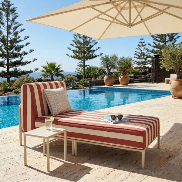Gestreifte Gartenliege mit Beistelltisch und großem Sonnenschirm auf einer Terrasse am Pool.